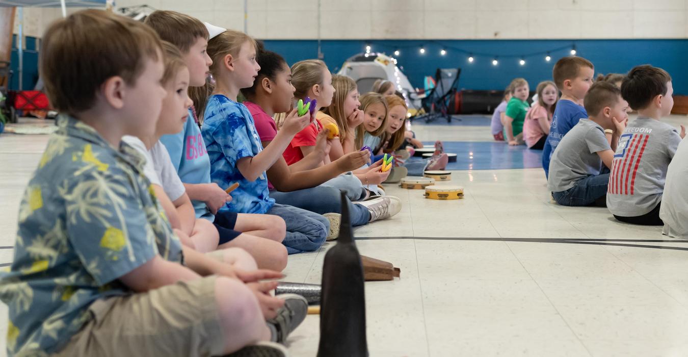 Group of children sitting in a line, playing instruments together.