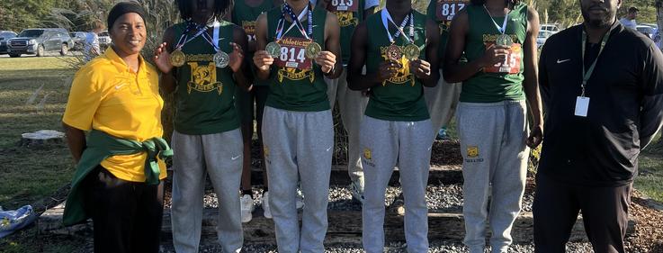 Coach and six athletes pose together with medals at an outdoor event.