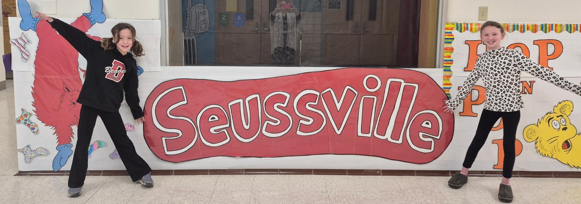Two children posing beside a large sign reading 'Seussville' in a school setting.