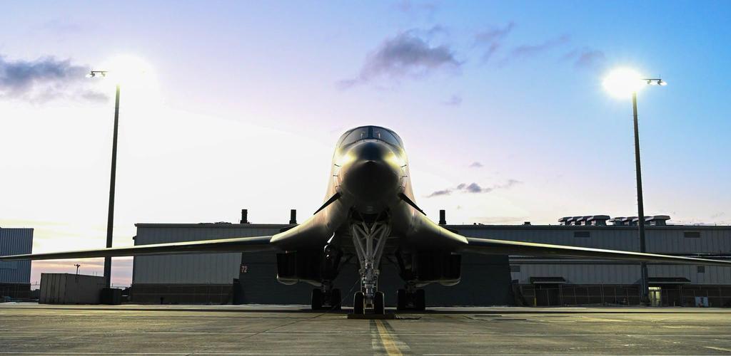 A large military aircraft at sunset, illuminated by surrounding lights.