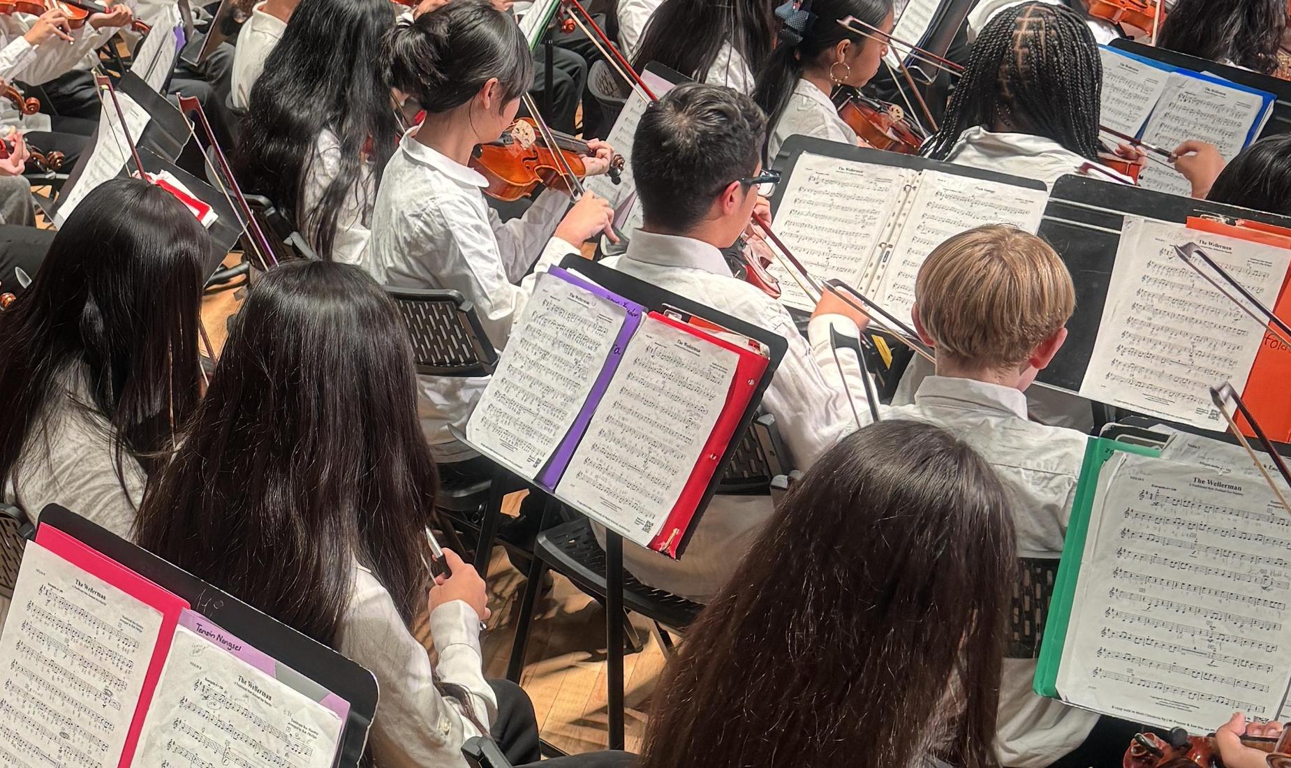 Students on a stage playing violins.