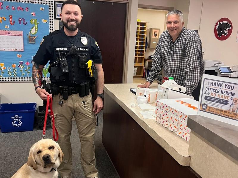 A police officer poses with a dog in a school office setting.