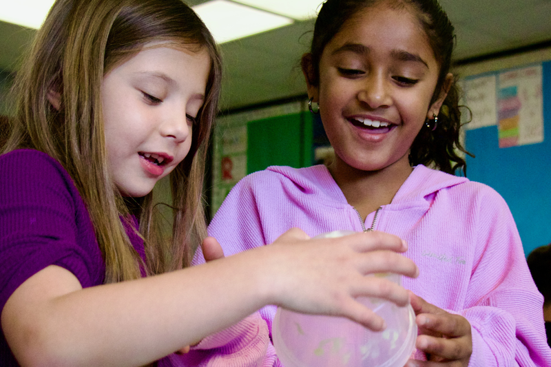 Two young children look excited as they pour contents out from a bowl