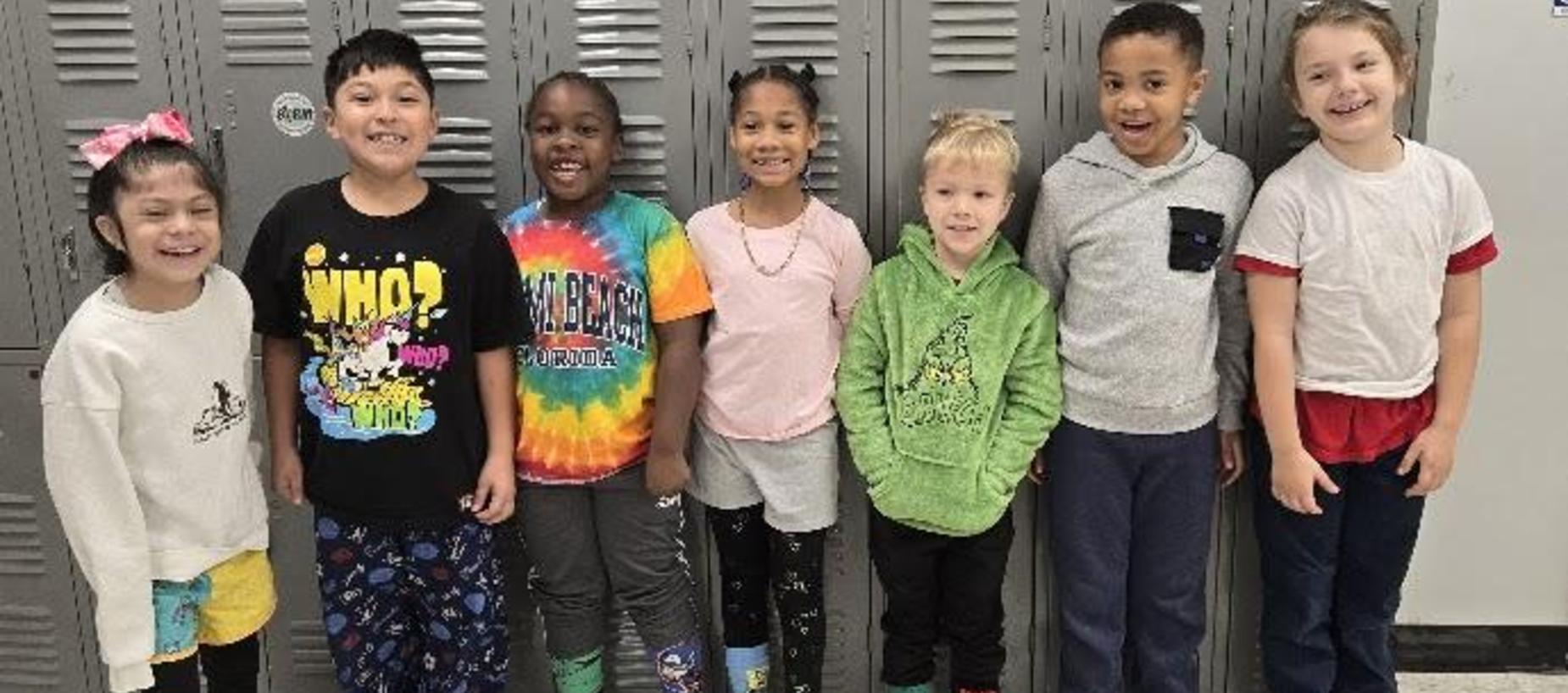 A group of eight smiling children standing in front of lockers.