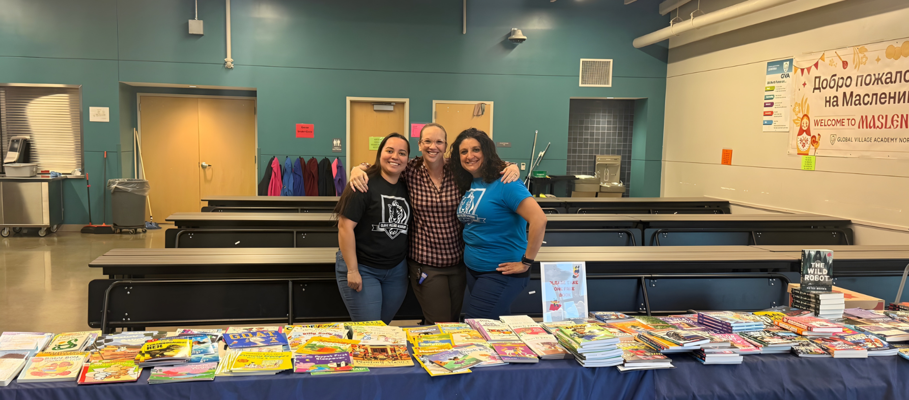 Three smiling individuals pose in front of a table filled with books.