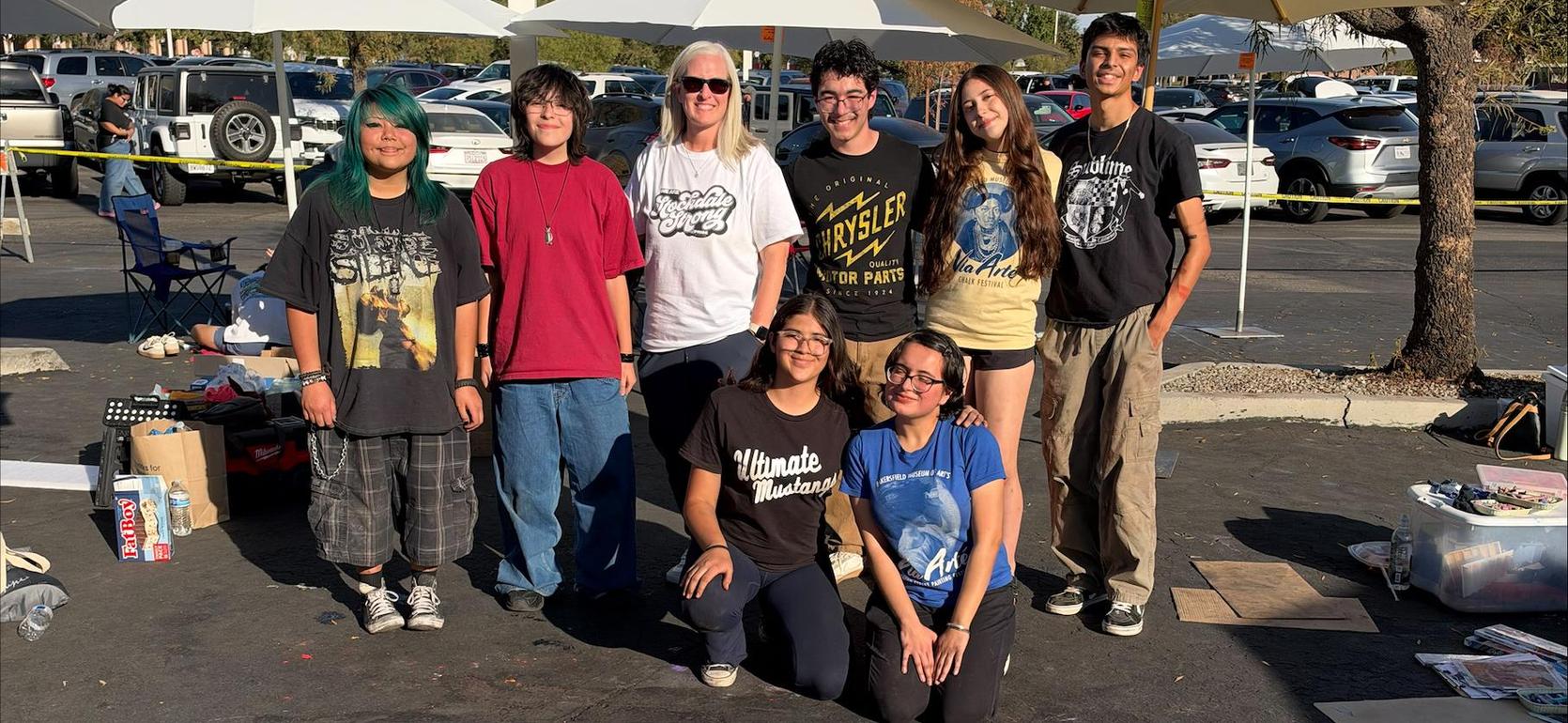 Group of artists posing with chalk art in a parking lot.