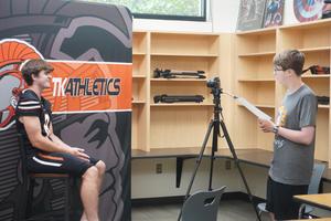 A student interviews and films one of the football players.