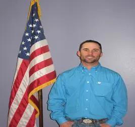 Man in a blue shirt stands next to an American flag.