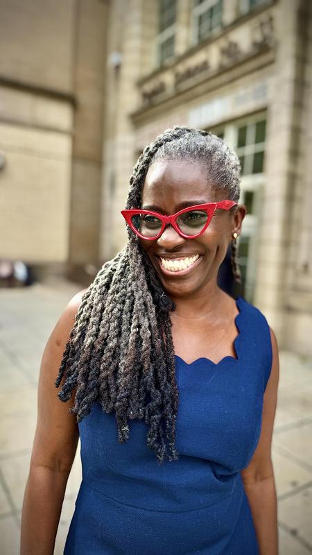 Principal with a bLUE dress and red glasses smiling in front of the school building