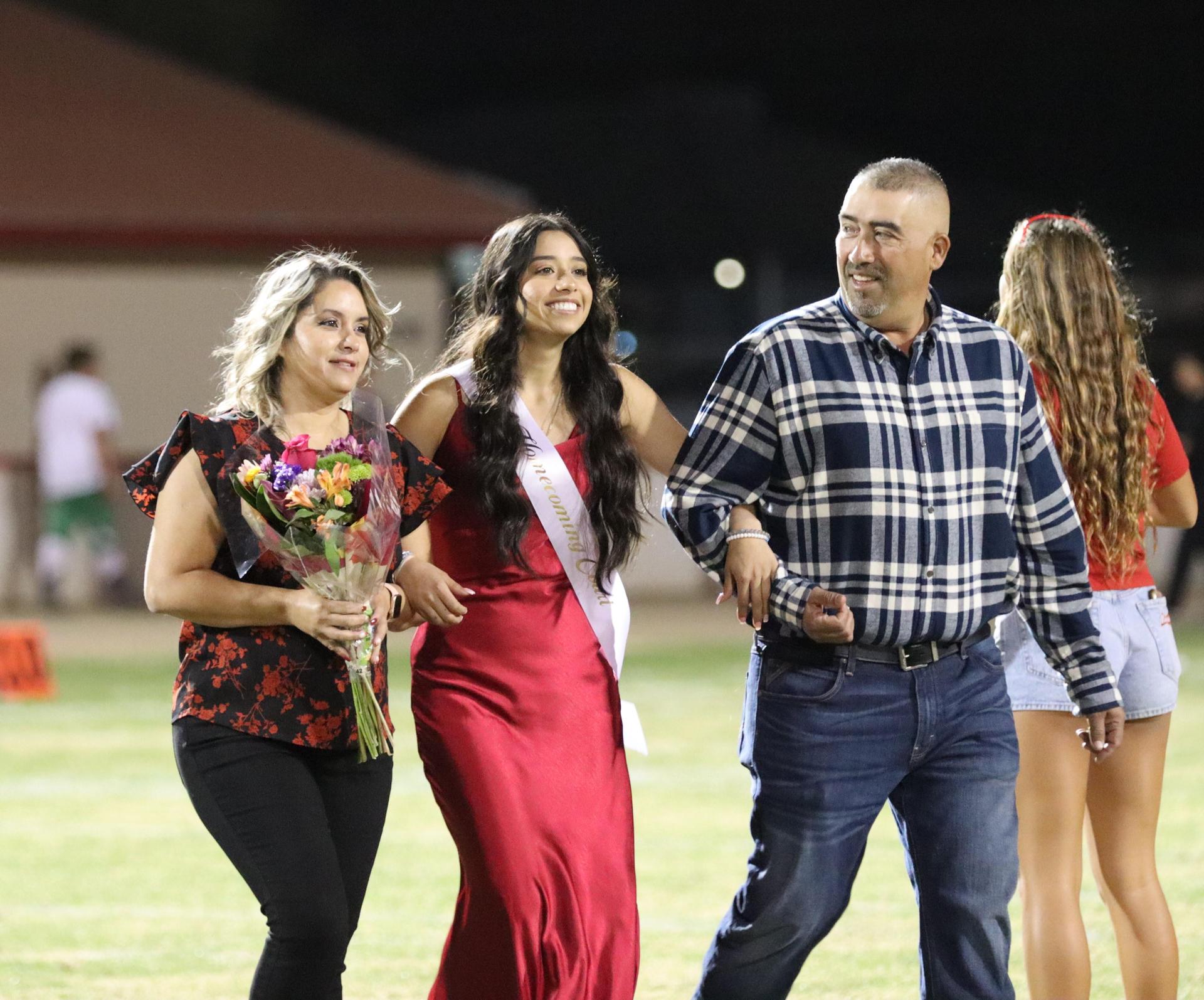 homecoming king and queen candidates walking across the field with their escorts