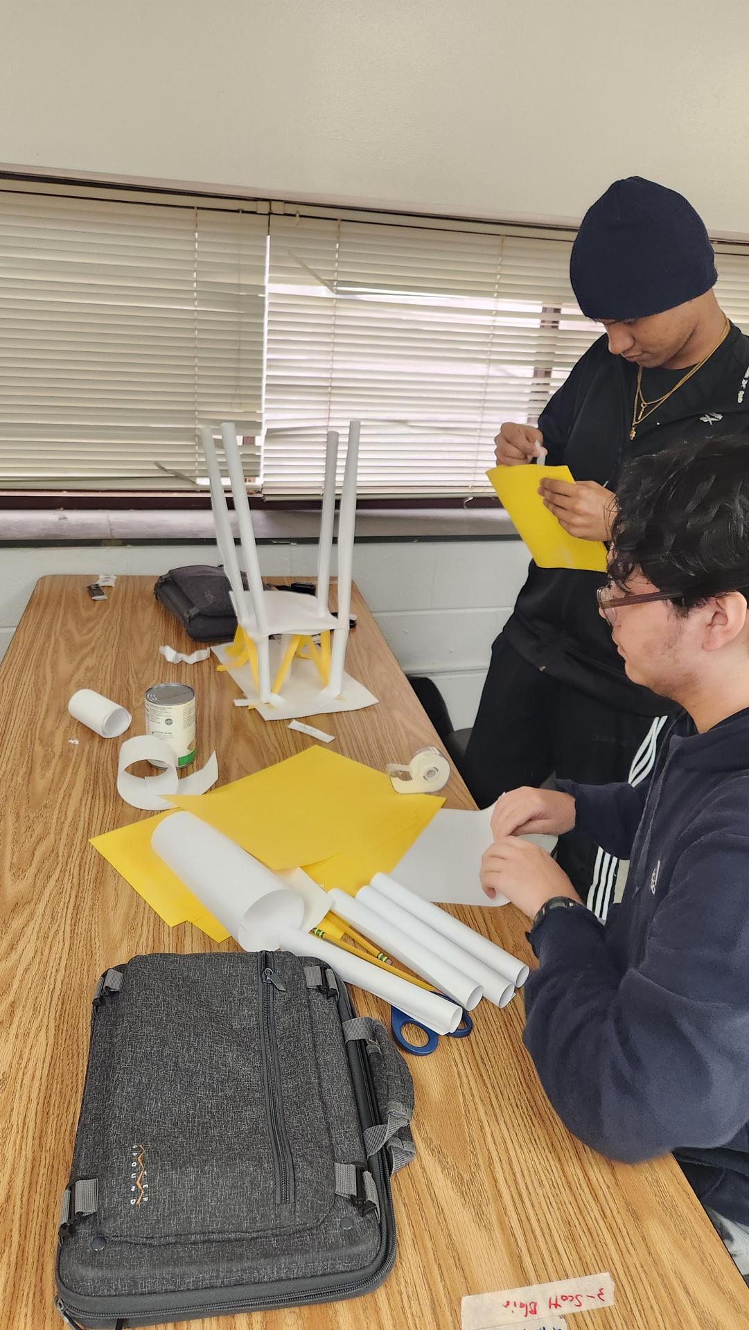 Two students collaborating on a project at a table with materials.