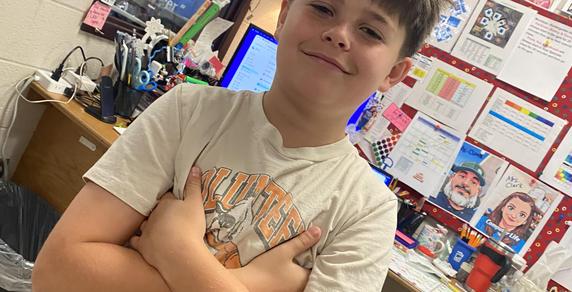 Smiling boy crossing his arms in a classroom setting.