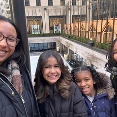 Group of four people smiling outdoors near a building with a skating rink.