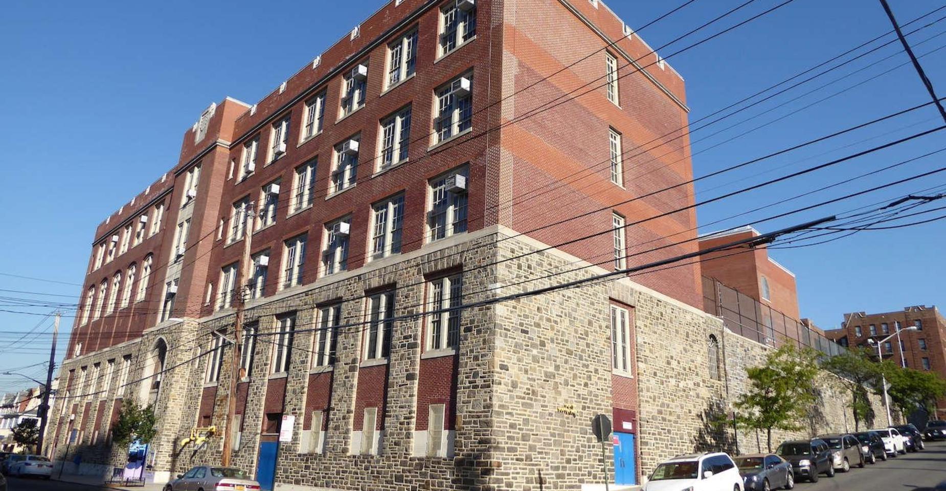 Corner view of a multi-story brick school building with a stone base.