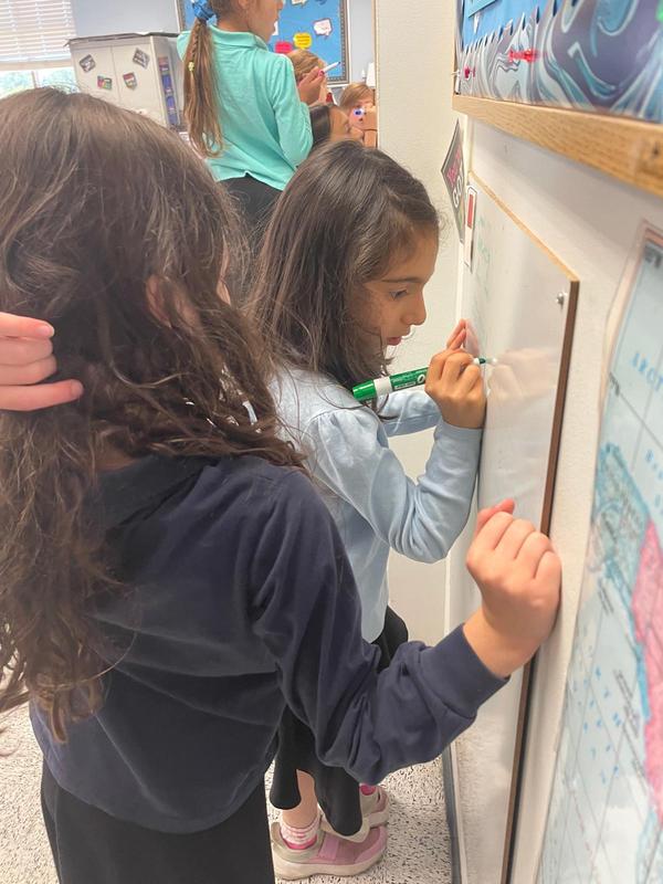 Two third grade girls work together on a non-vertical surface board.
