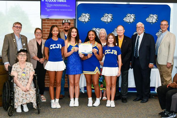 A group of dancers and cheerleaders in uniform with school board members, smiling and holding an award