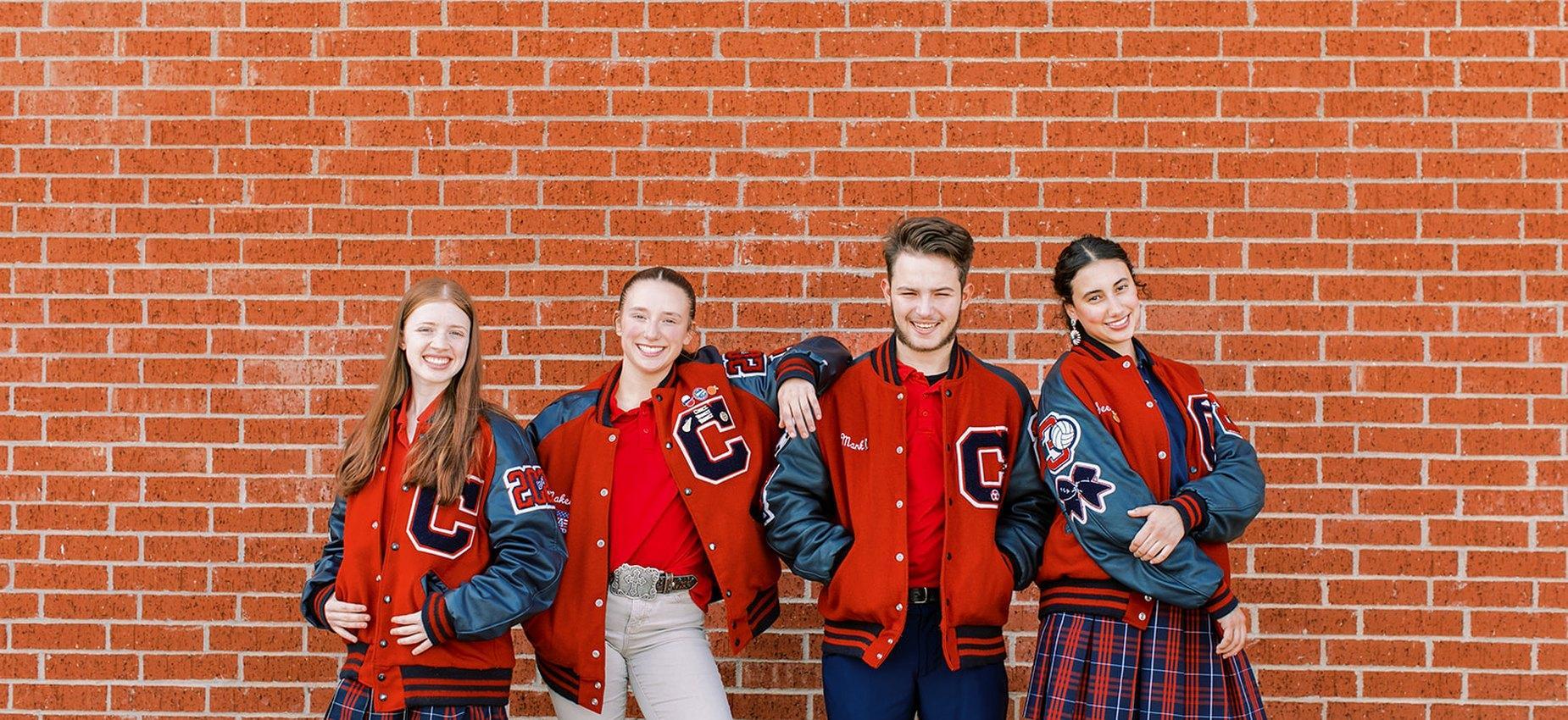 Founders Classical Academy of Corinth student athletes in letter jackets in front of a brick wall