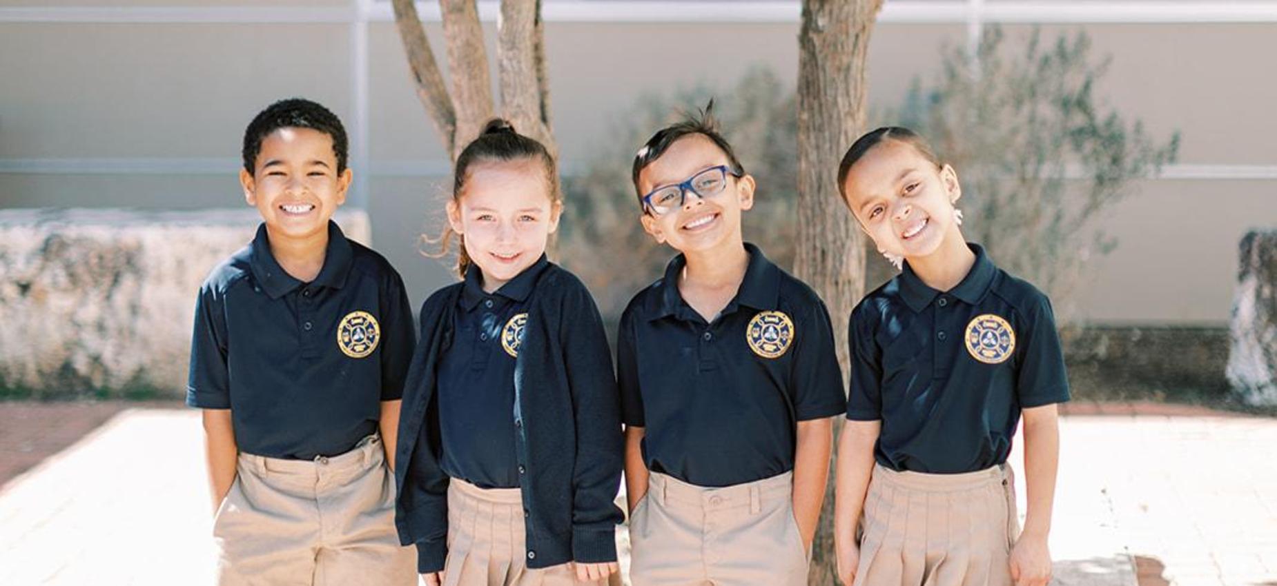 Four smiling elementary students in navy uniforms stand together outside