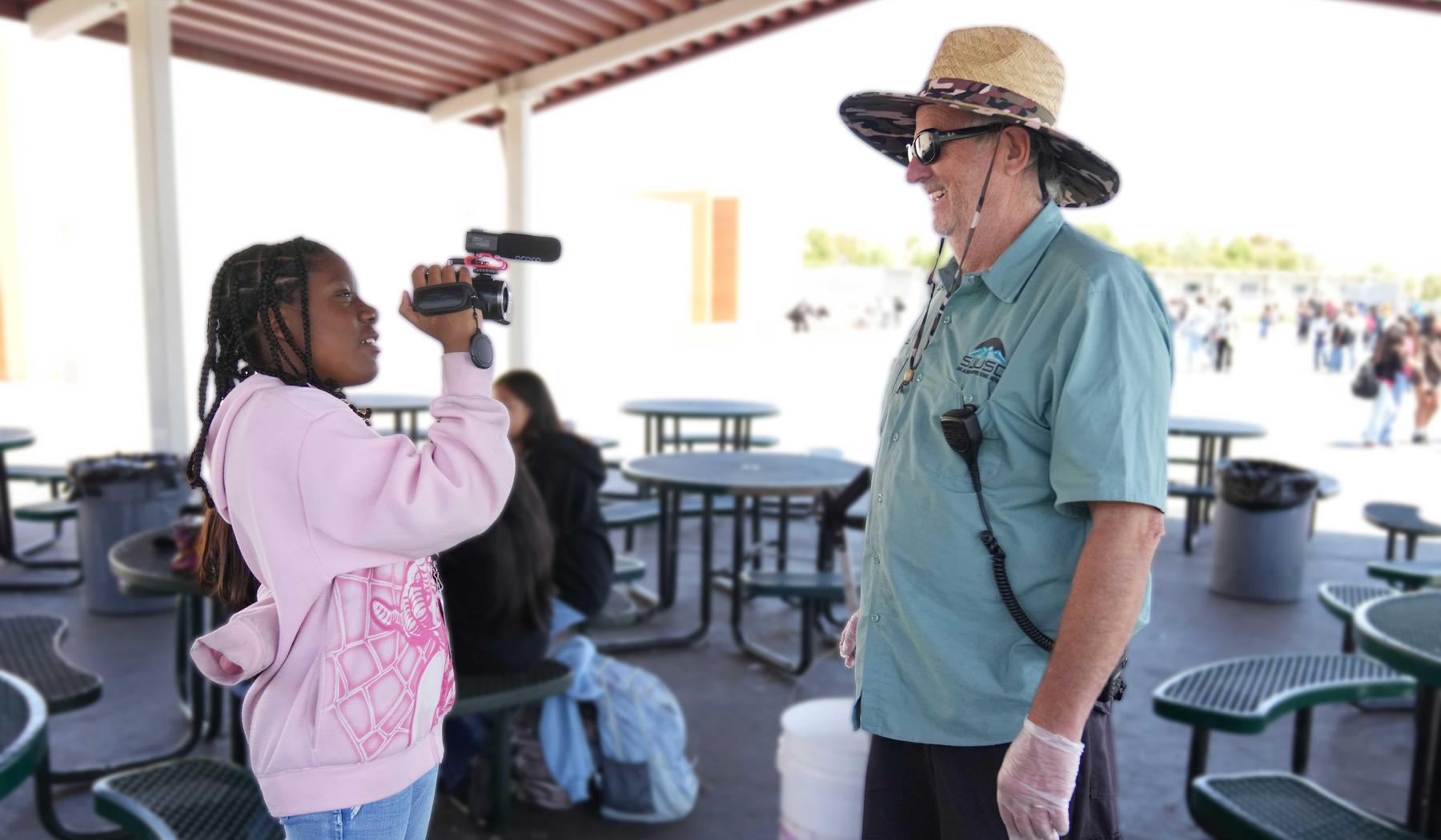 Student holding a camera interviewing a custodian