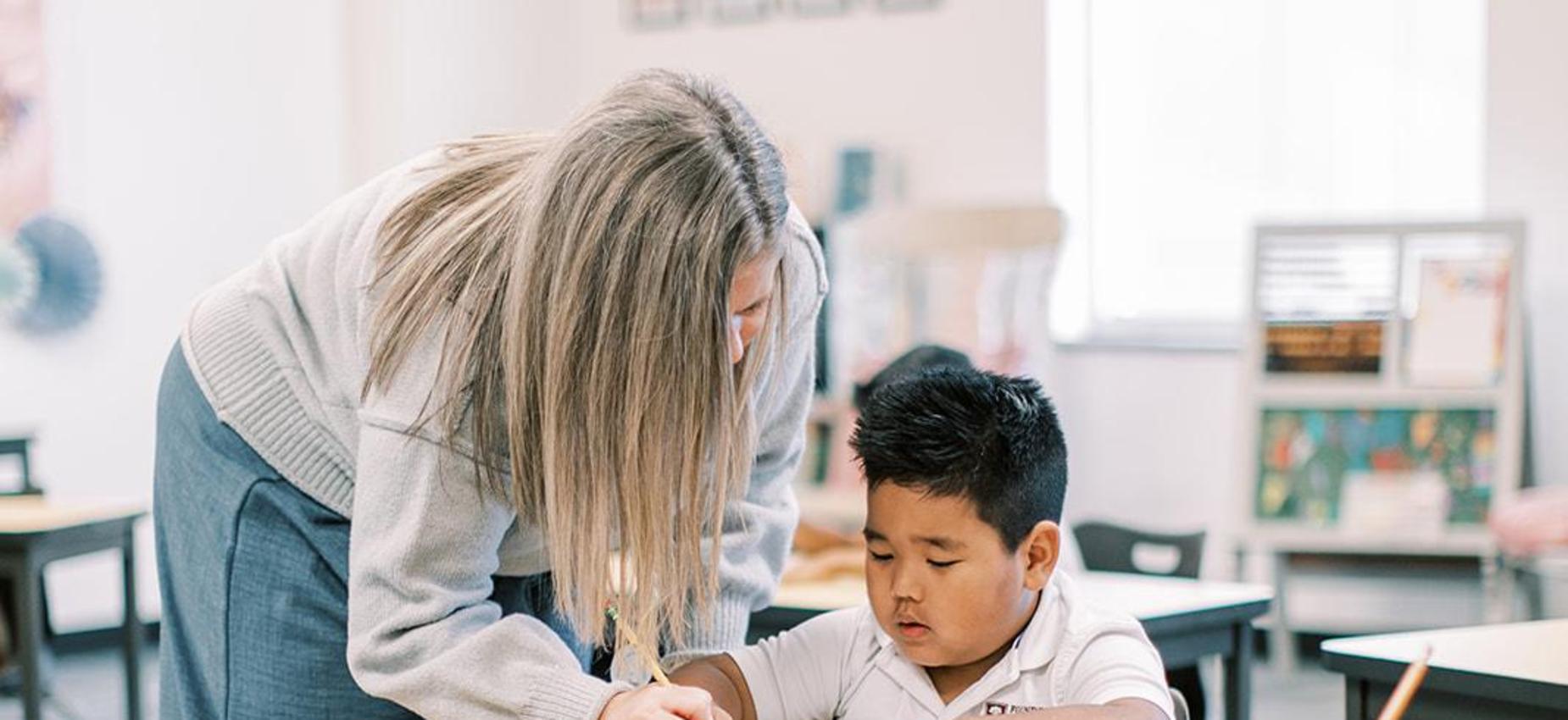 Teacher leaning over to help a student with his work at his desk