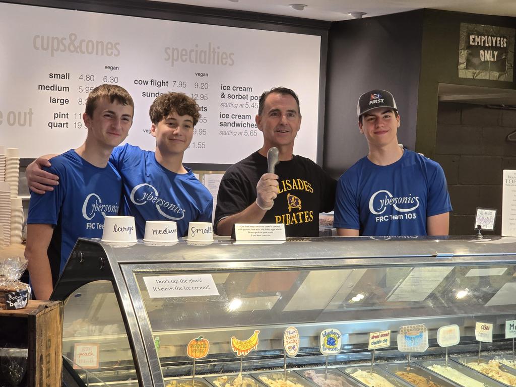 Mr. Heffernan holding up an ice cream scoop and standing with three Cybersonics team members behind the counter at Owowcow.