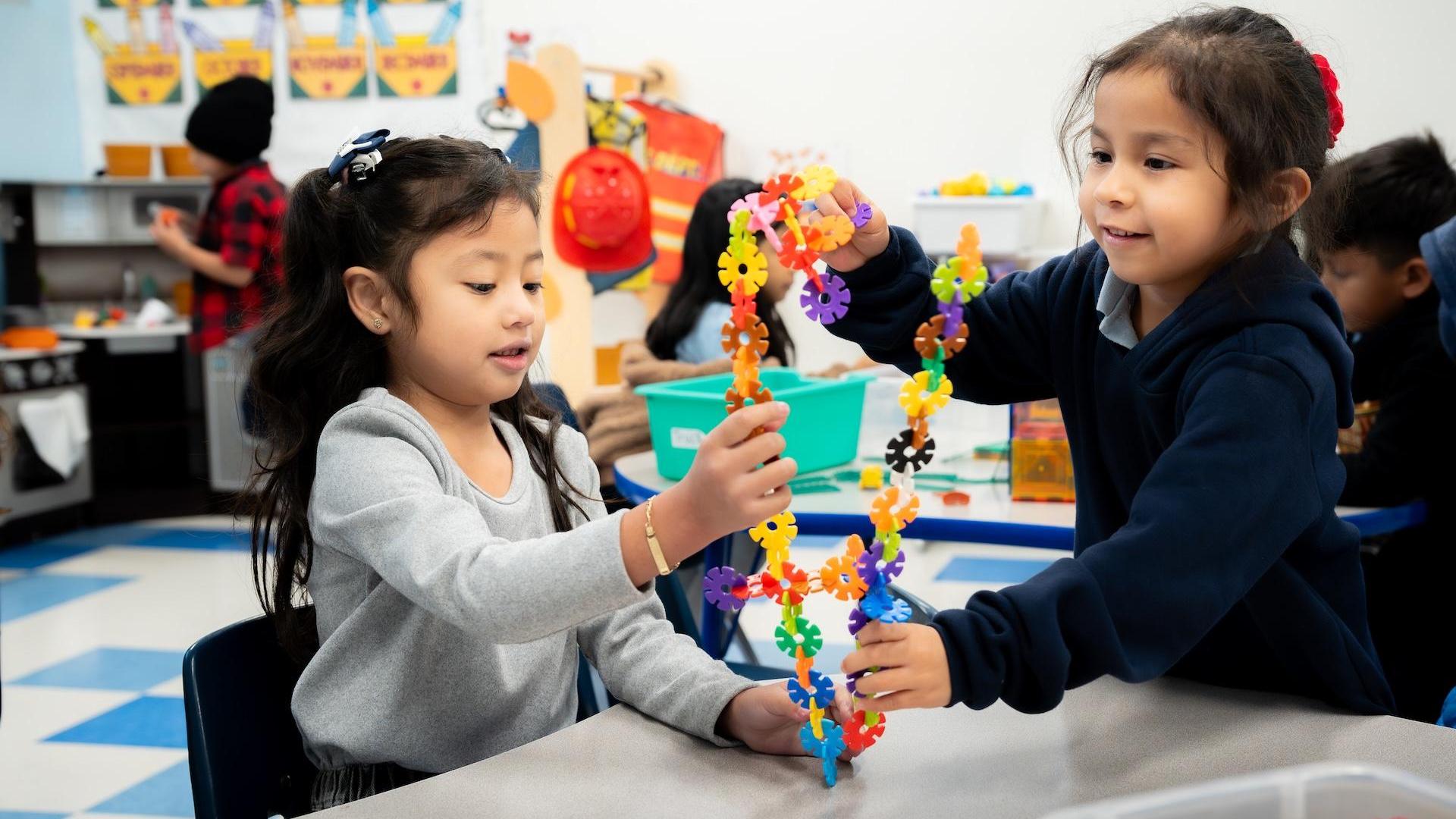 Two girls collaborating and building with colorful plastic flower-shaped pieces.