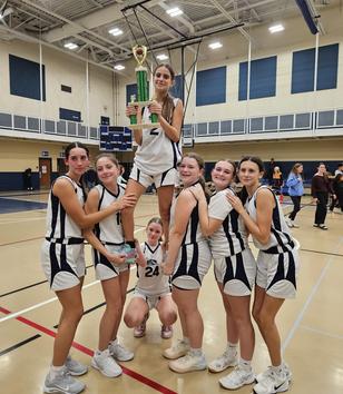 A basketball team celebrates with a trophy, one player elevated by the rest.