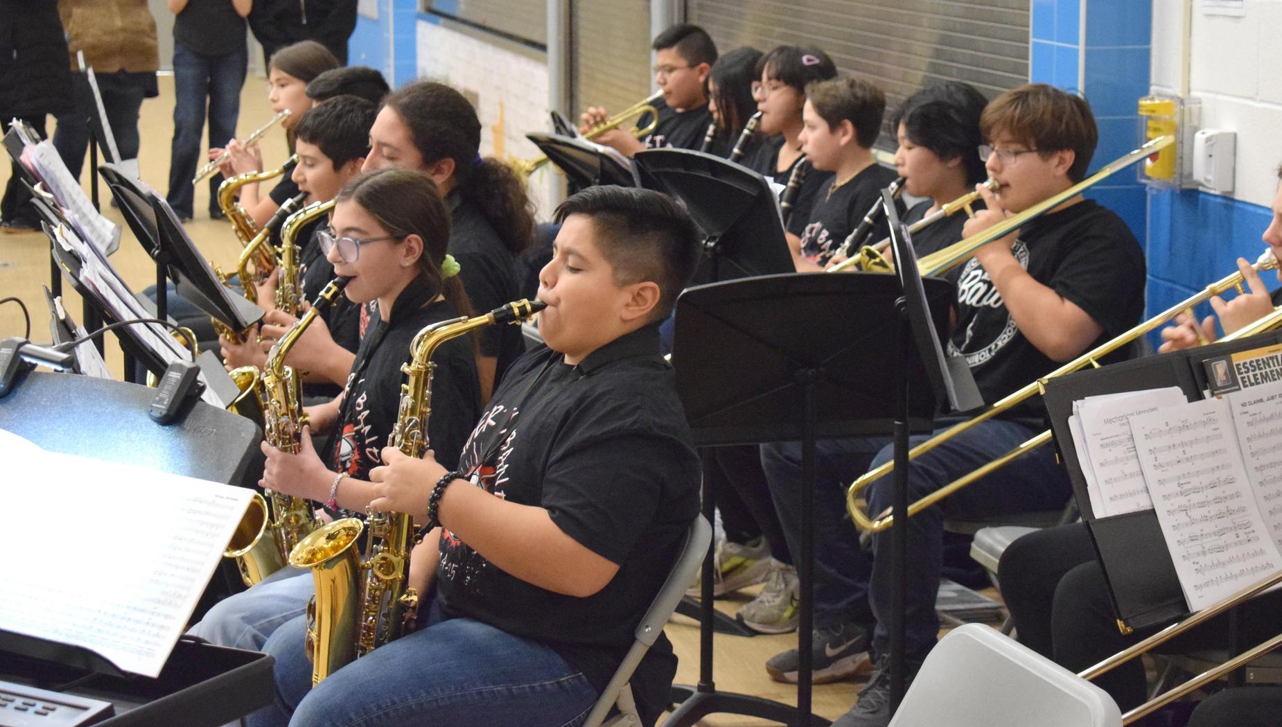 A youth saxophone ensemble playing music in a gym setting.