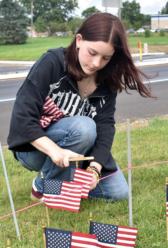 A person kneels, placing American flags on the grass.