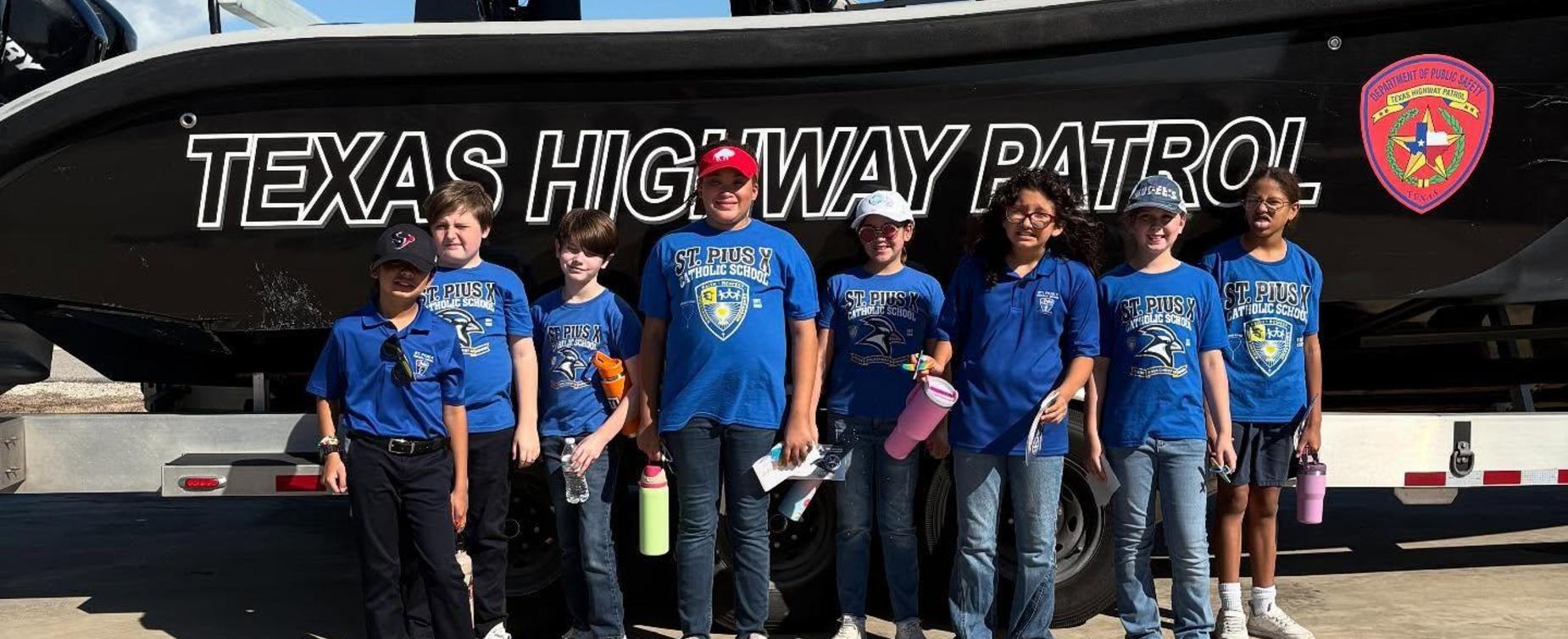 A group of children in blue shirts standing in front of a Texas Highway Patrol boat.