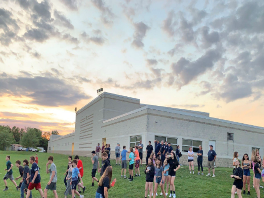 Students standing outside on the lawn next to the school with a beautiful sky overhead.