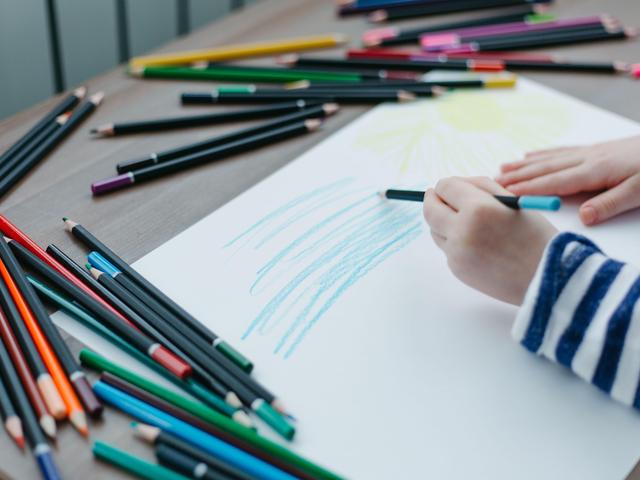 A child's hand drawing with colored pencils scattered around on a table.