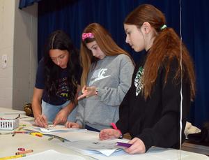 a college student helping two girls complete a writing activity