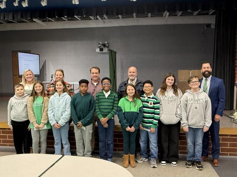 children wearing green and blue standing in front of adults smiling