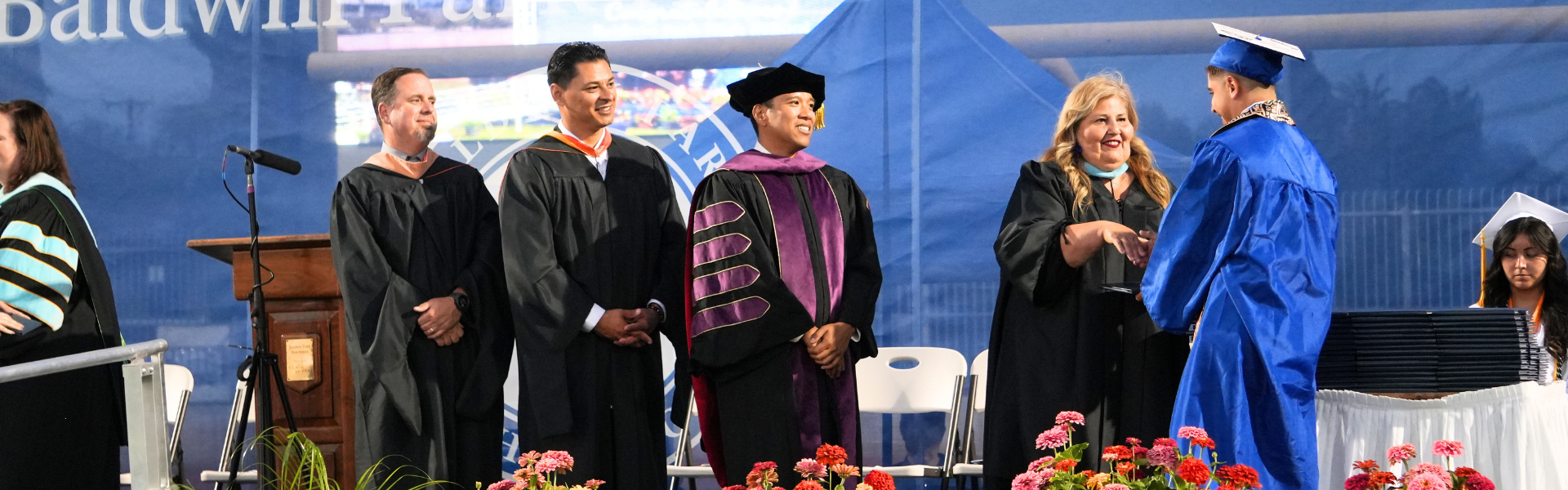 Graduation ceremony with graduates receiving diplomas on stage.