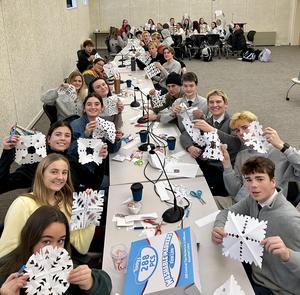 Group of students making snowflakes at a long table in a classroom.