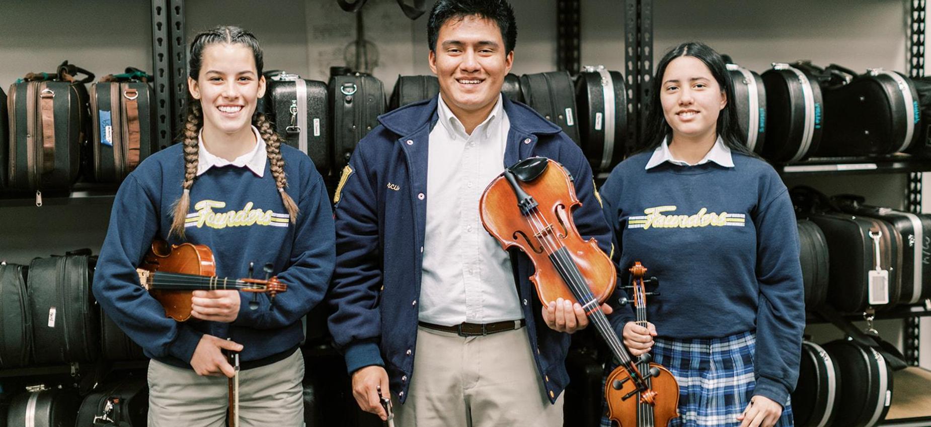 Music teacher stands with two students holding a violin and viola in the orchestra room