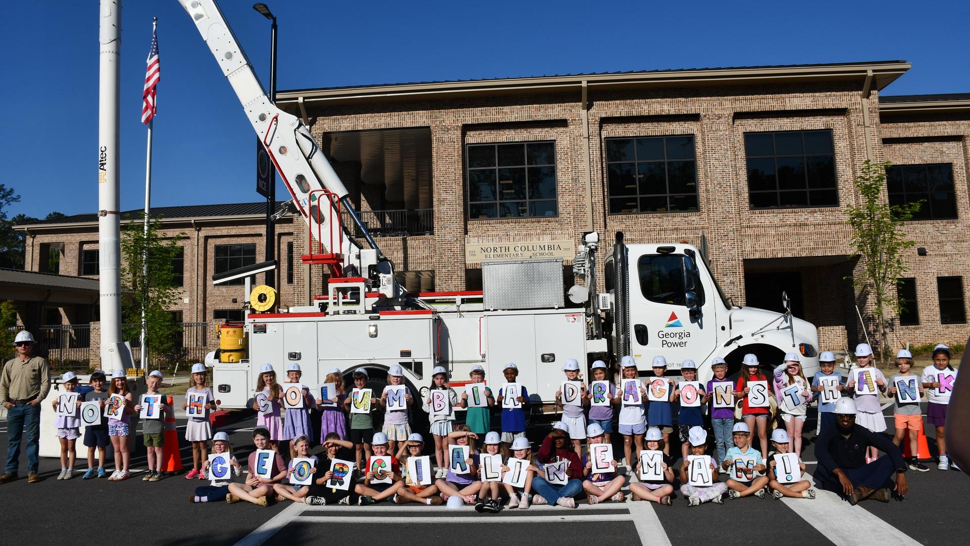 Students holding banners in front of a utility truck and a large tree.