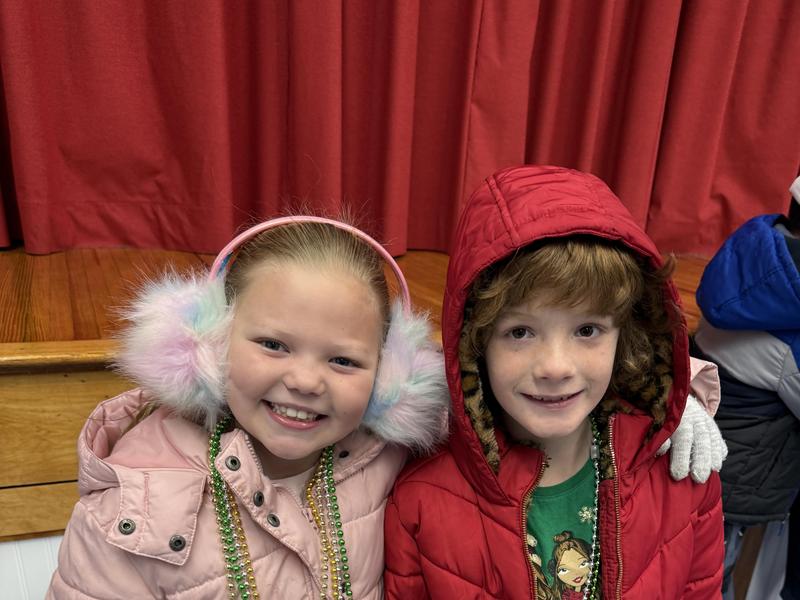Two kids posing with festive accessories, wearing winter coats and happy expressions.