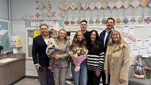 Board and exec cabinet members stand with Courtney in her classroom. Courtney is holding a large bouquet of flowers