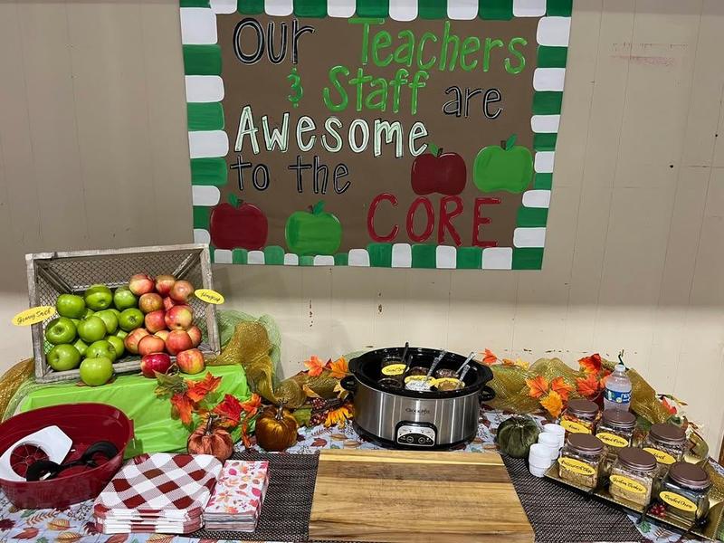 A colorful display of fall-themed decorations, food, and apples with a supportive sign.