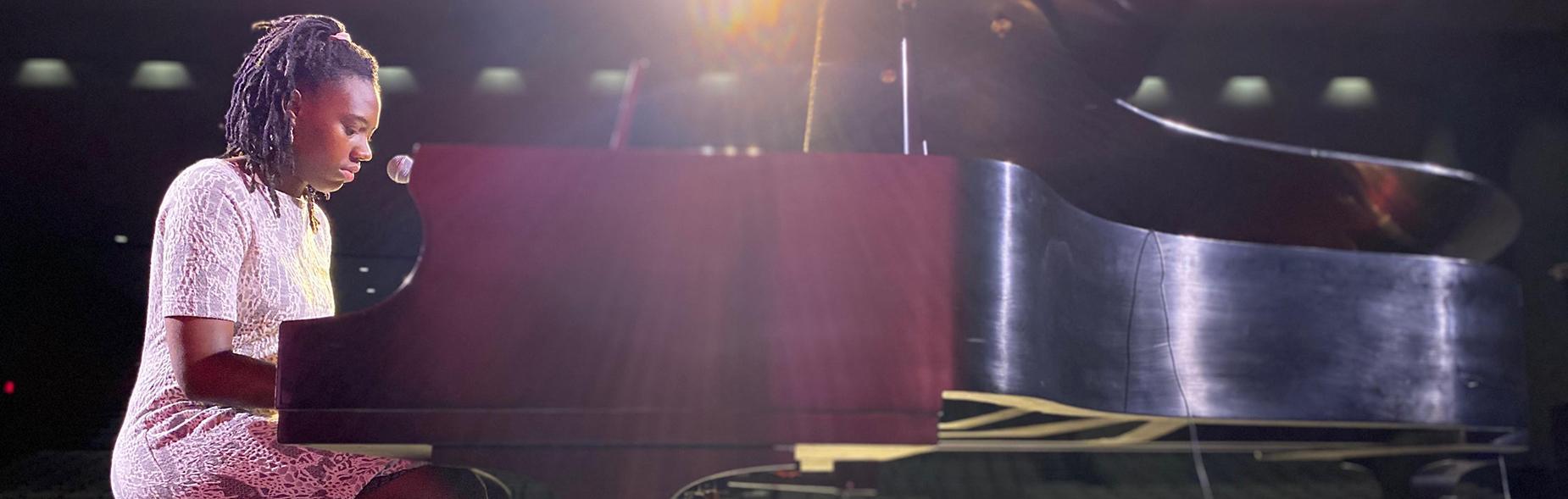 Student playing the piano in a concert hall.