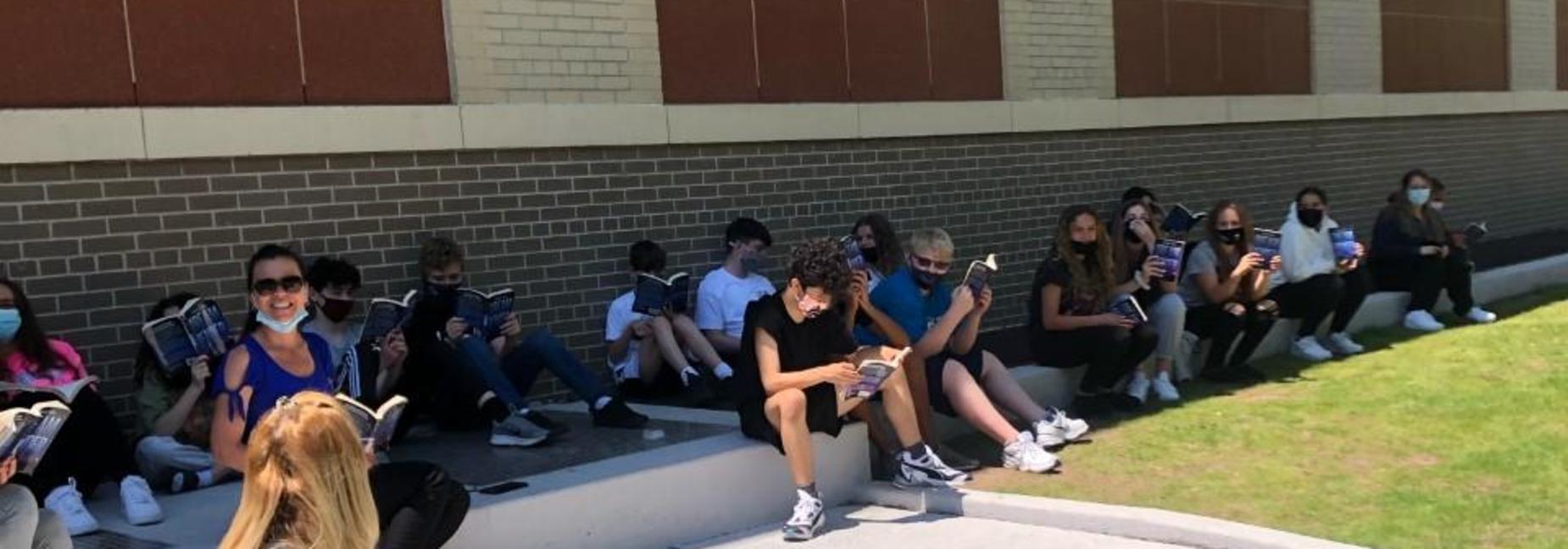 Mrs. Sutera and 8th grade students reading outside of the school