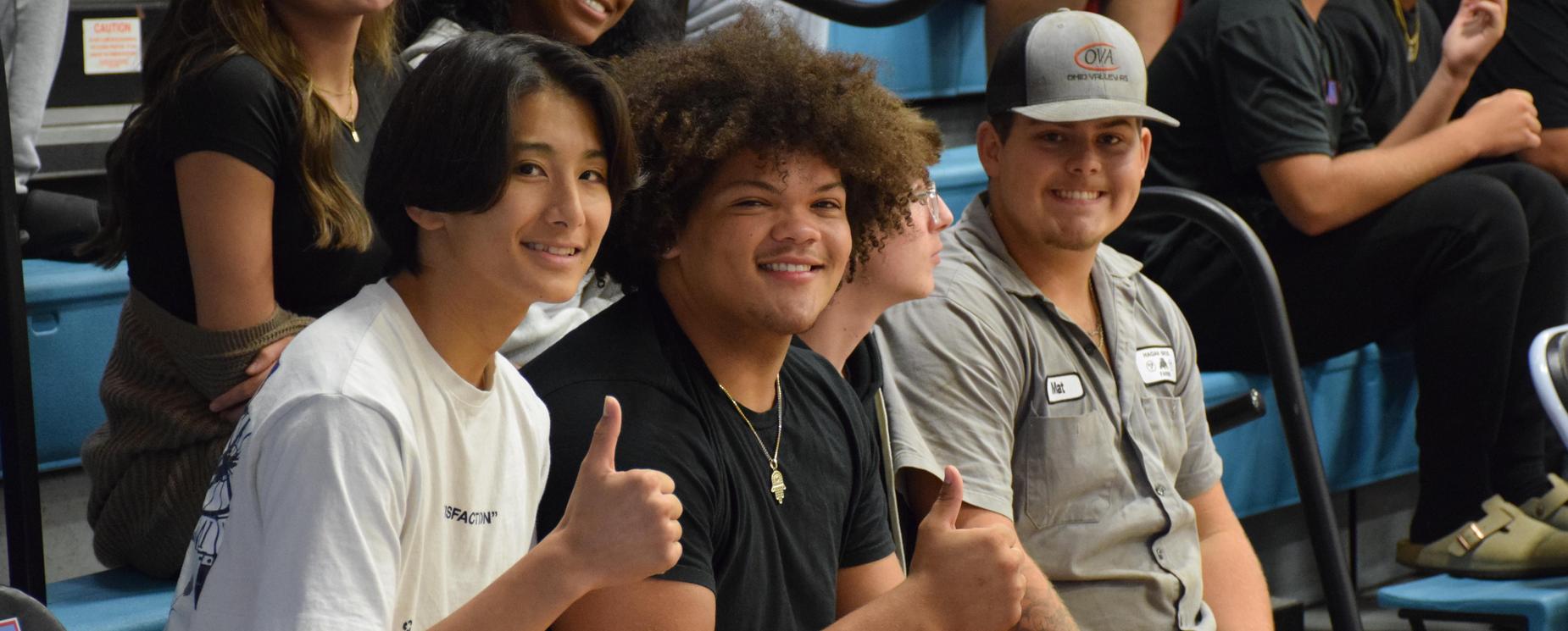 High school students smiling in bleachers and showing thumbs up
