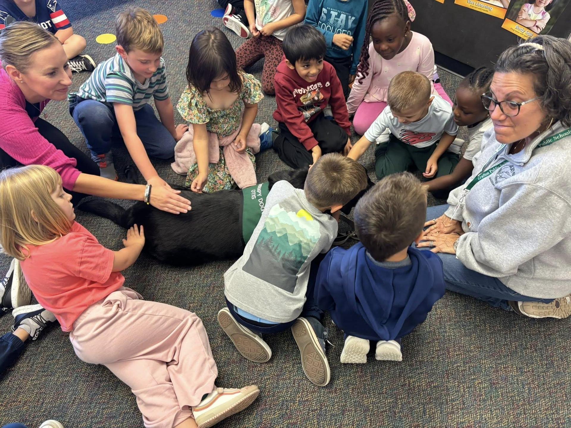 students sitting on the floor and petting a therapy dog brought to the classrooms