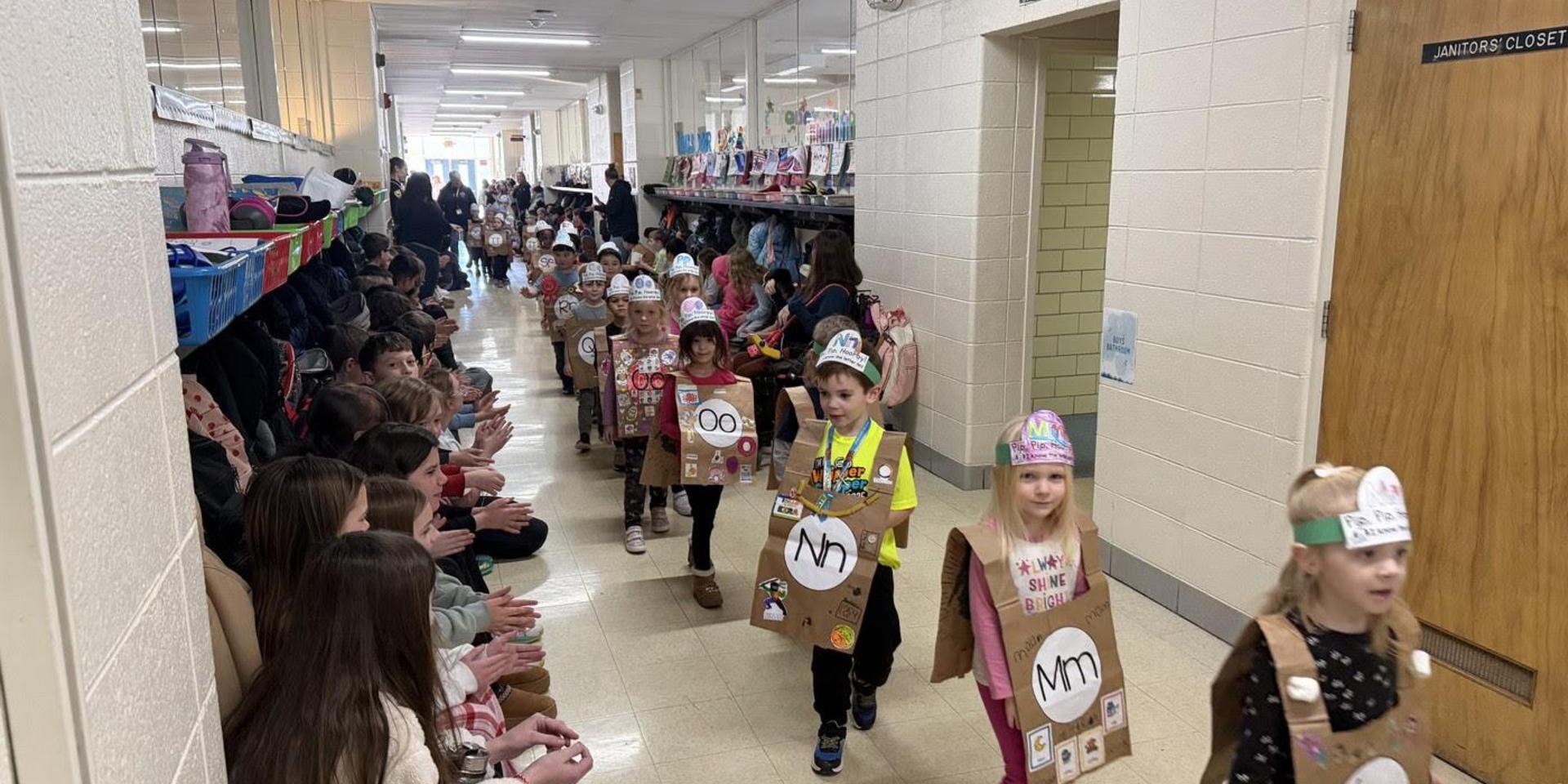 Children in costumes marching down a school hallway during an event.