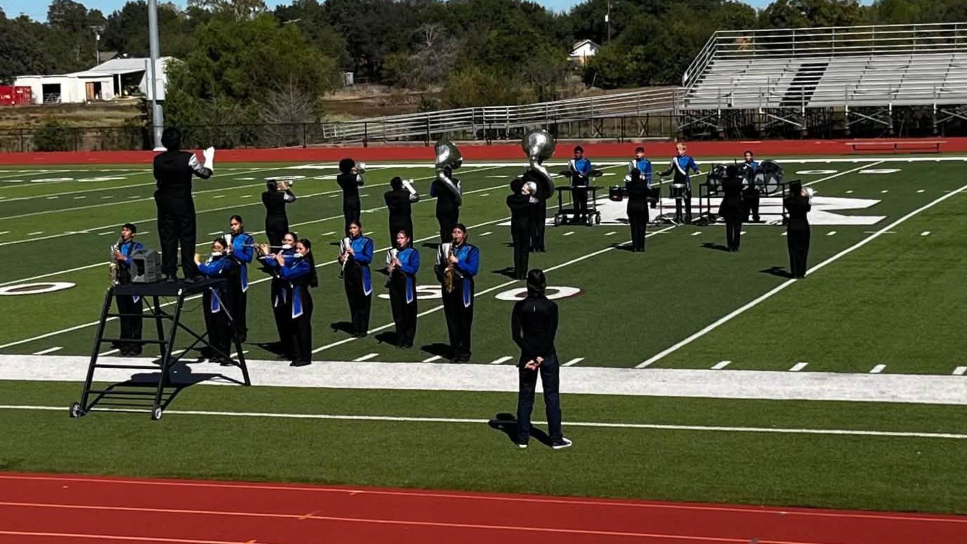 Marching band performing on a sports field with stands in the background.