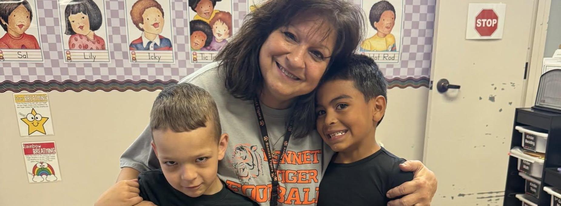 A woman with two boys posing together in a classroom setting.