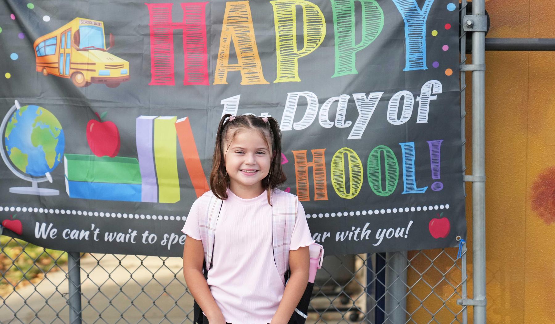 girl standing in front of happy first day of school sign
