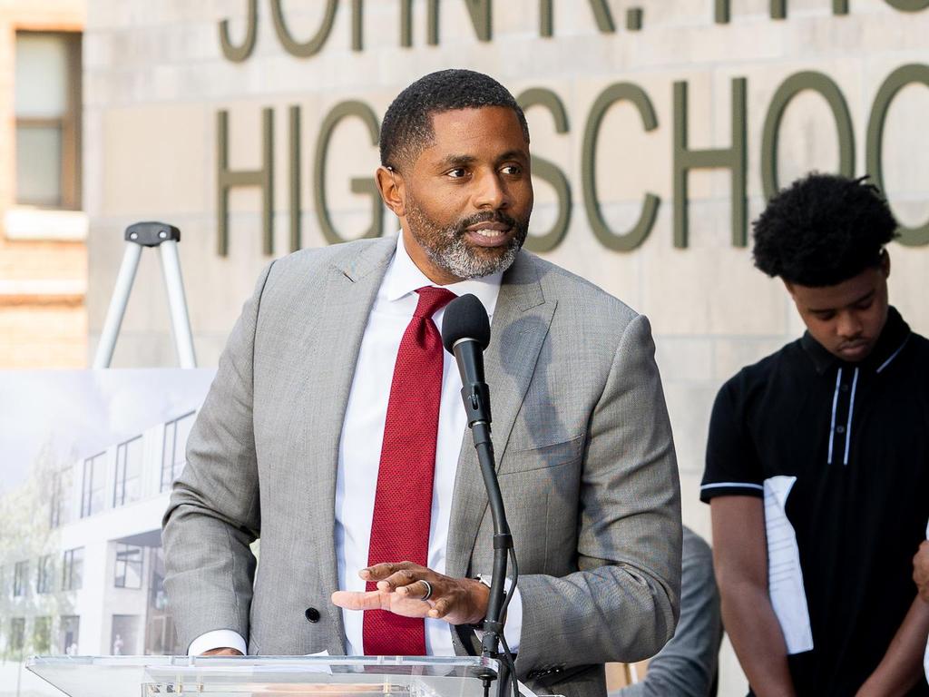 A man in a suit addresses a crowd outside John R. Thompson High School, with a young man beside him.